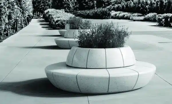 Vista de un banco de hormigón circular modular con jardinera integrada en un paseo peatonal.